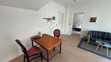 A room with a dining table, two chairs, a sofa, a bed, and a painting on the wall.