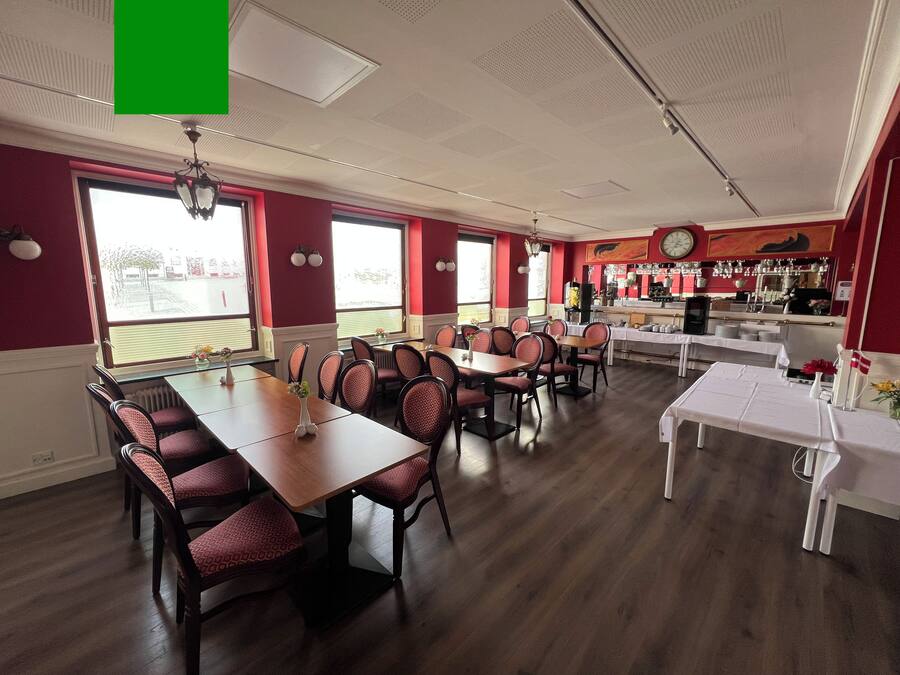 A dining area with multiple tables and chairs, a bar area with shelves of glasses and bottles, and large windows providing natural light.