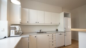 Una cocina moderna con armarios blancos, lavavajillas integrado, cafetera y refrigerador.