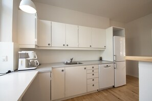 A modern kitchen with white cabinets, a built-in dishwasher, a coffee maker, and a refrigerator. - Det Gamle Rådhus (Grasten)