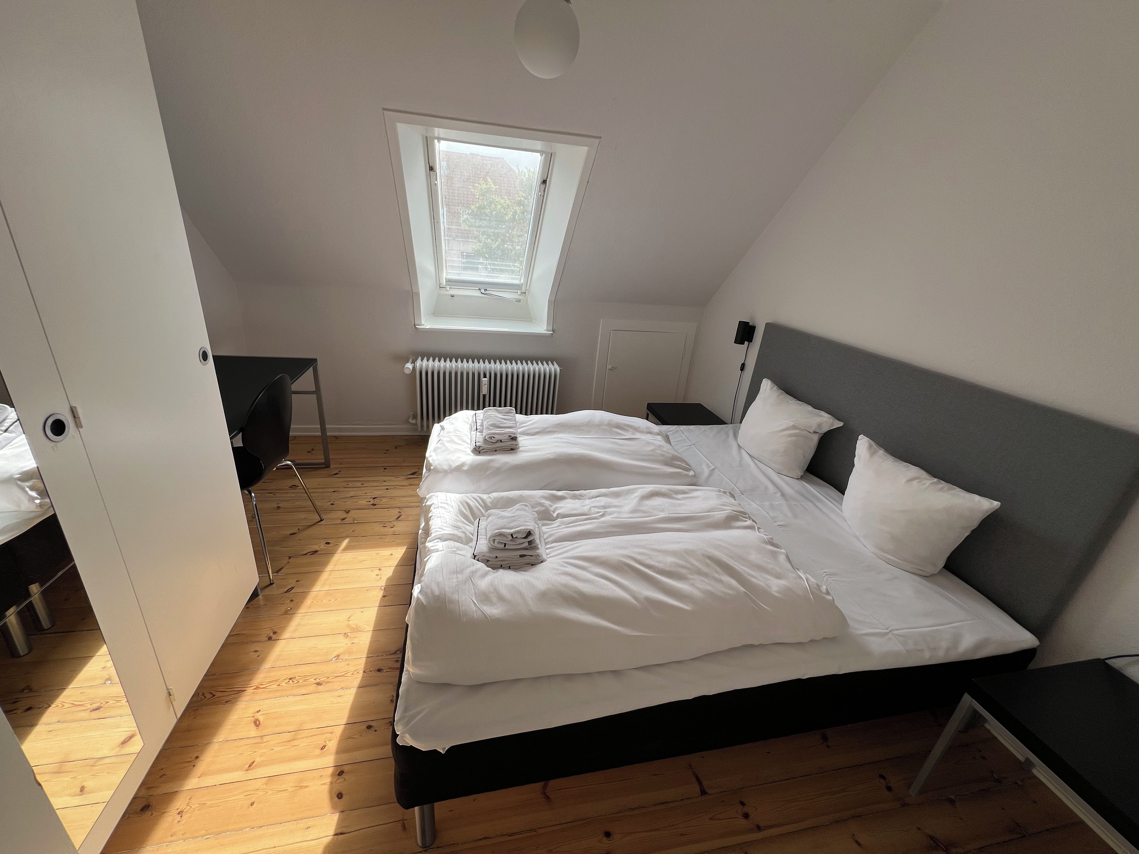 Un dormitorio con cama, escritorio, silla, radiador y ventana.
