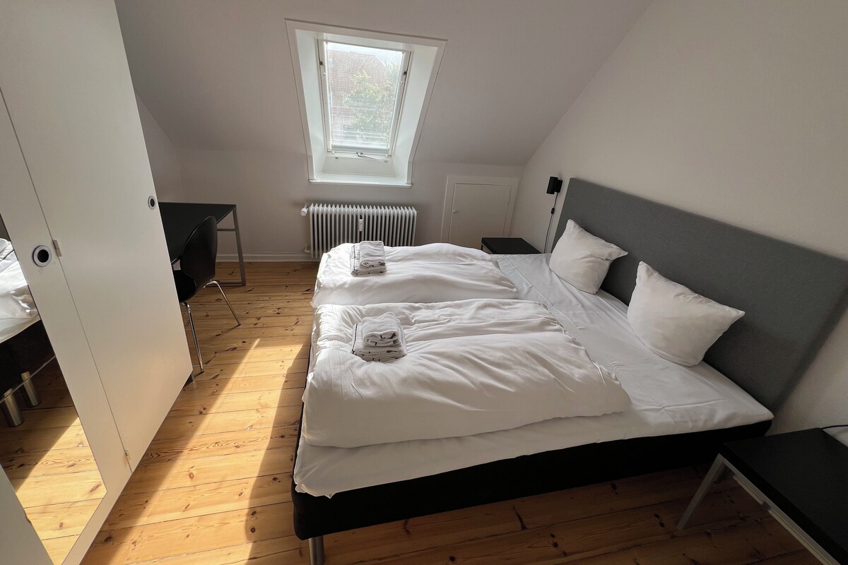 A bedroom with a bed, a desk, a chair, a radiator, and a window.
