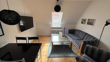 A modern living room with a black dining table, two chairs, a glass coffee table, a striped sofa, and a black pendant light.