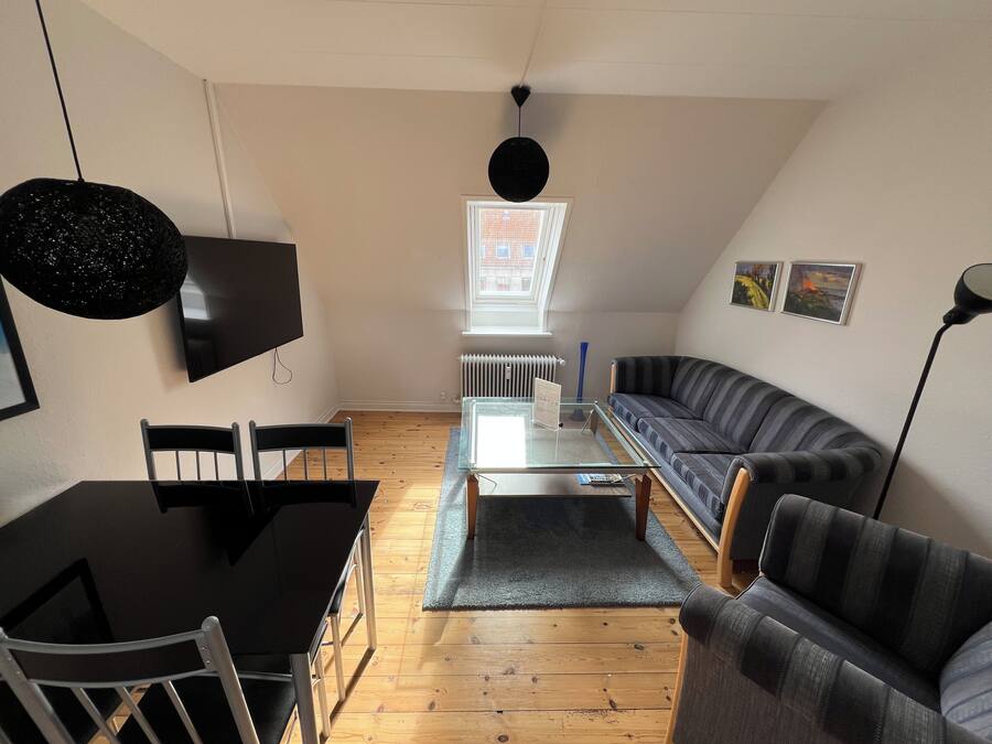 A modern living room with a black dining table, two chairs, a glass coffee table, a striped sofa, and a black pendant light.