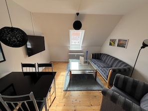 A modern living room with a black dining table, two chairs, a glass coffee table, a striped sofa, and a black pendant light. - Det Gamle Rådhus (Grasten)