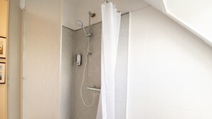 Una ducha con puerta de vidrio, un cabezal de ducha de mano y un panel de control en la pared.