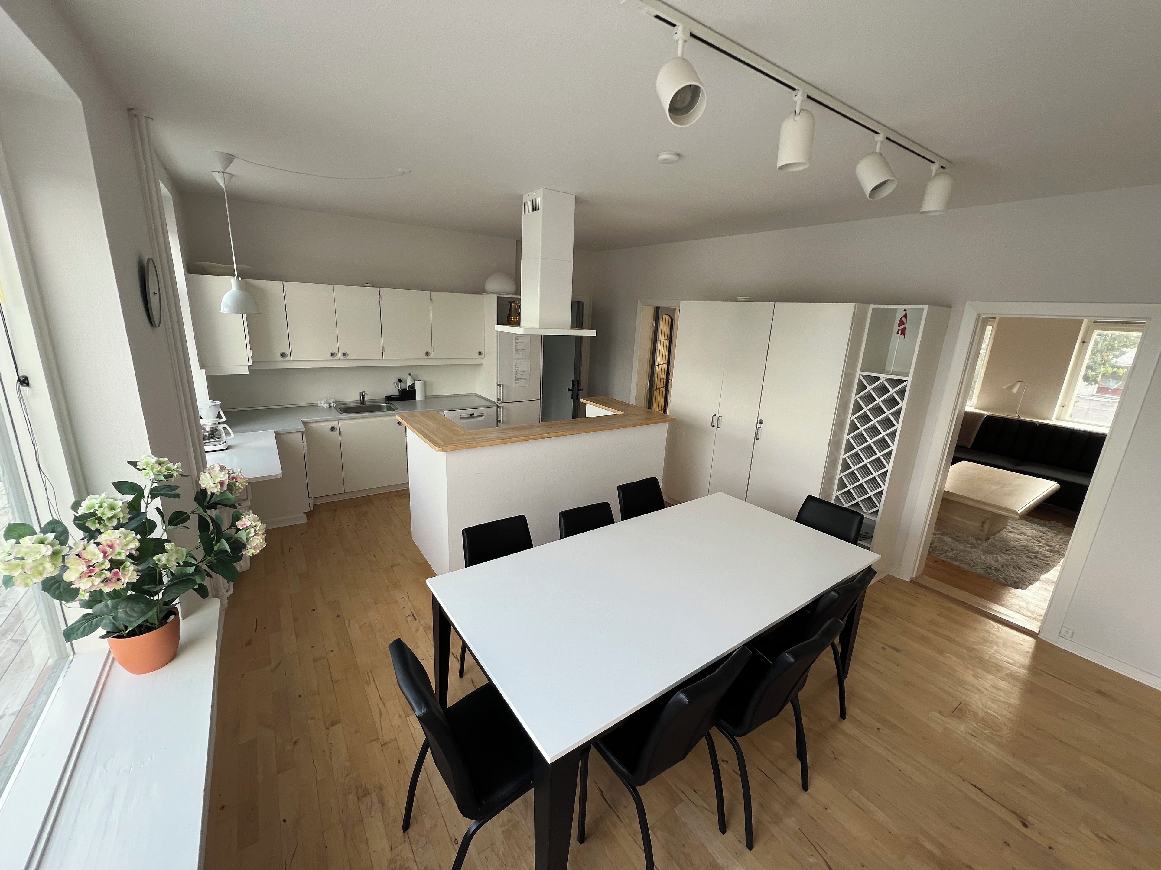 Een moderne keuken met witte kasten, een centraal eiland en een eetgedeelte met een witte tafel en zwarte stoelen.