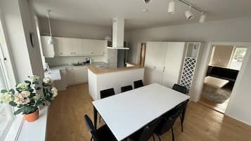 Een moderne keuken met witte kasten, een centraal eiland en een eetgedeelte met een witte tafel en zwarte stoelen.