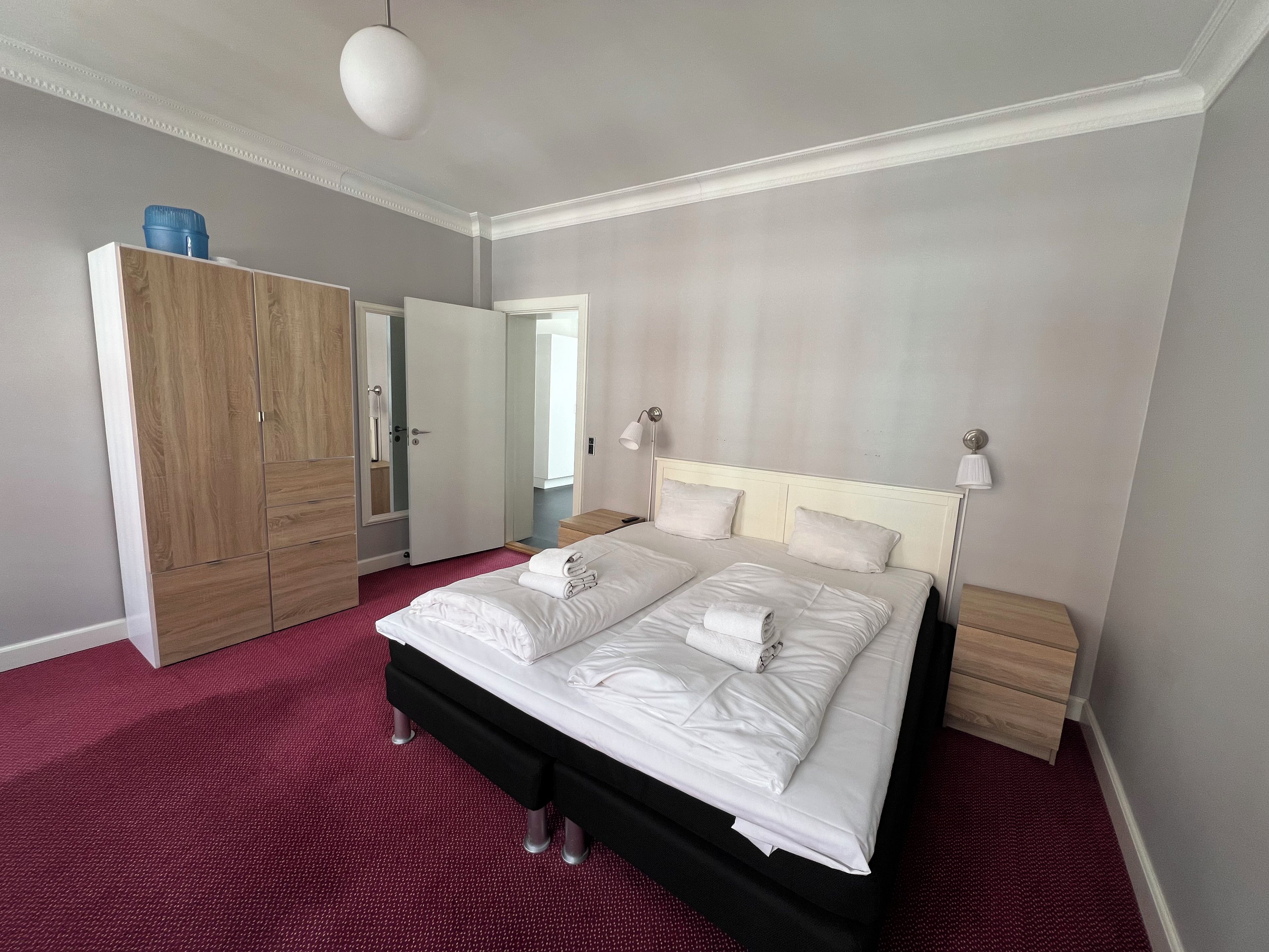 A hotel room with a large bed, a wardrobe, a mirror, and a bedside lamp.