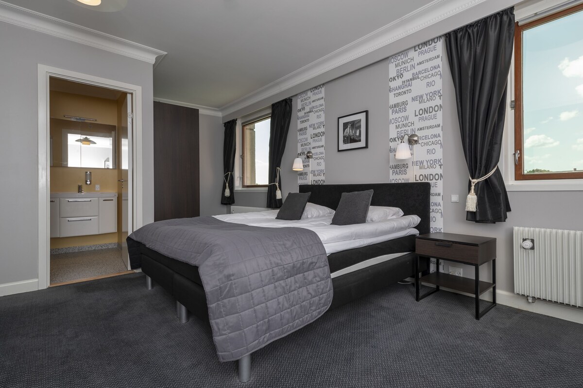 Una camera d'albergo moderna con un letto grande, un comodino, un armadio e una finestra con tende.