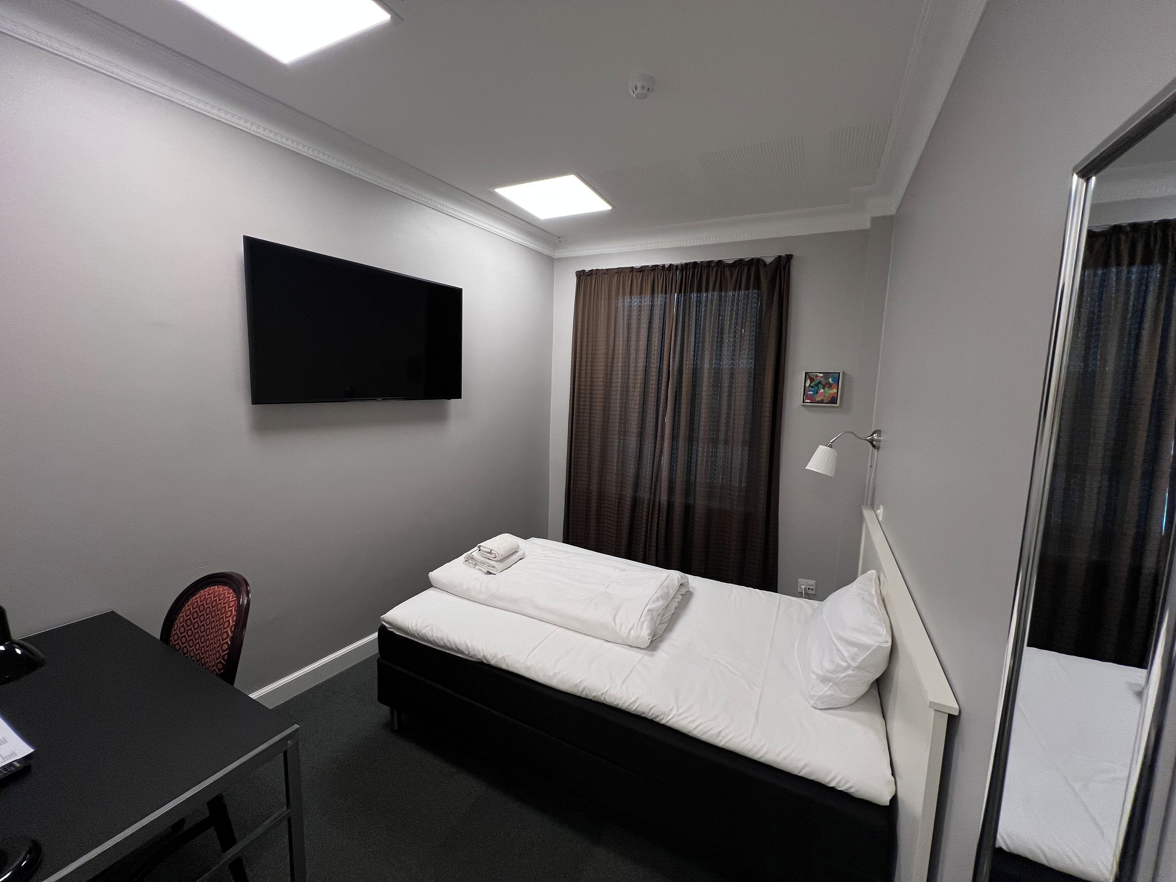Una habitación de hotel con una cama, un escritorio, una silla, un televisor de pantalla plana, una ventana con cortinas y una lámpara de noche.