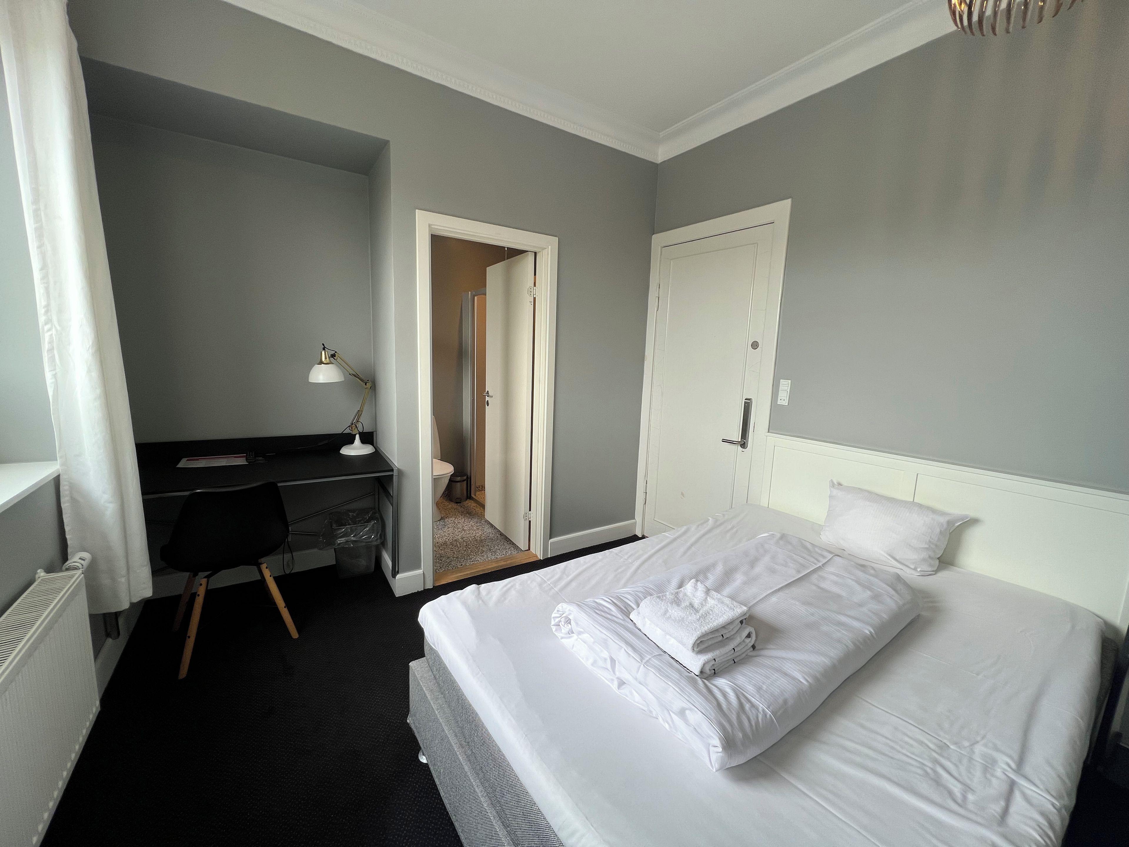 Une chambre d’hôtel comprenant un lit, un bureau, une chaise et une porte donnant accès à une salle de bain.