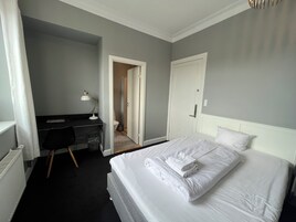 Habitación de hotel con cama, escritorio, silla y puerta que da a un baño.