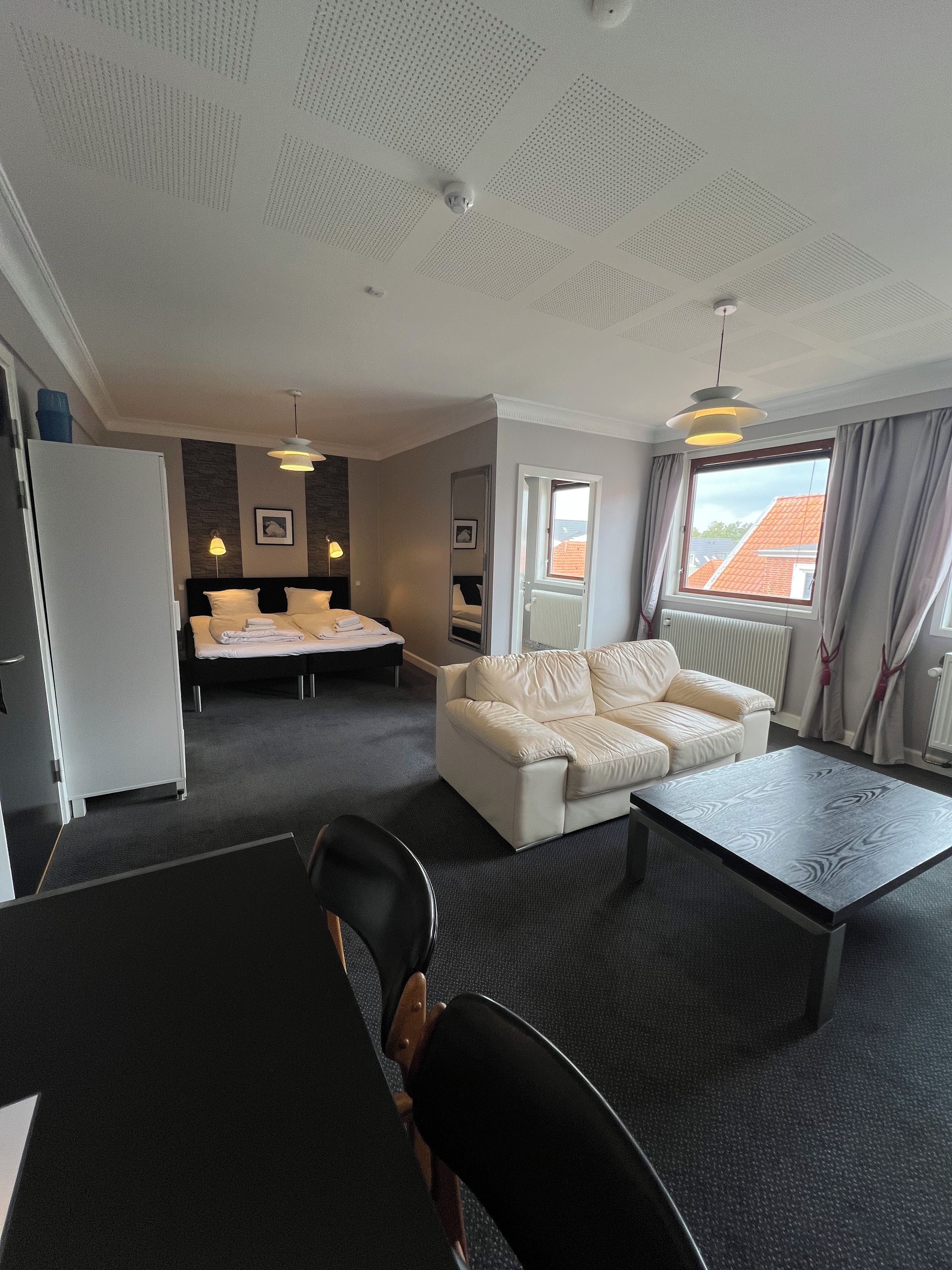 A hotel room with a bed, a sofa, a dining table, and a view of the outside.
