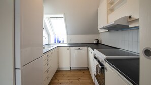 A compact kitchen with white cabinets, a dishwasher, a stove, and a window providing natural light. - Det Gamle Rådhus (Grasten)