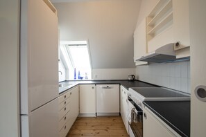 Una cucina compatta con mobili bianchi, lavastoviglie, fornello e finestra che lascia entrare luce naturale.