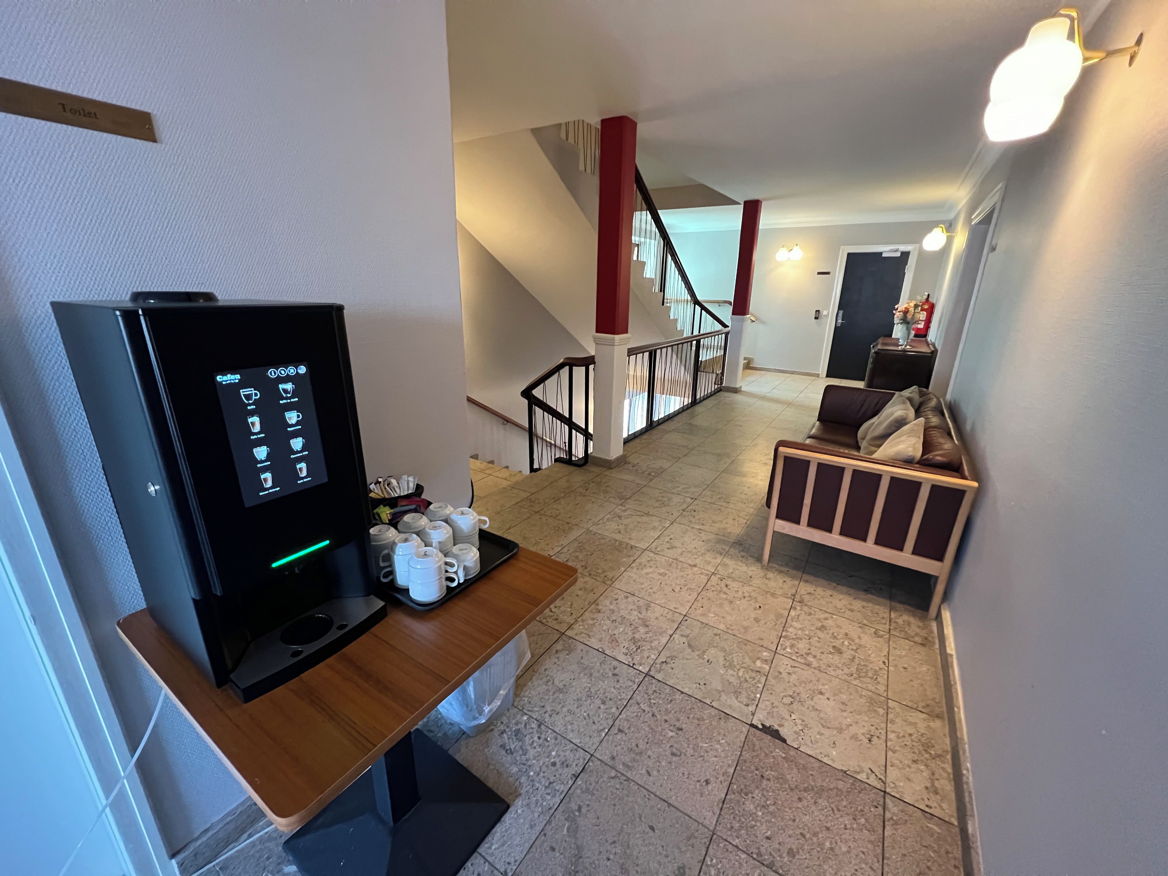 A hotel room with a coffee machine, a wooden table, a sofa, and a staircase.