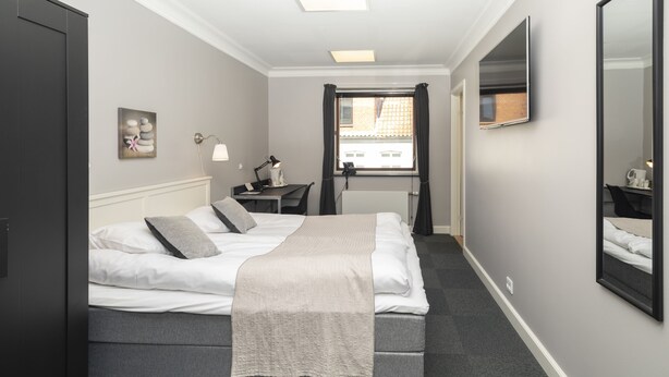 A neatly arranged hotel room with a bed, bedside table, lamp, and a window with curtains. - Det Gamle Rådhus (Grasten)