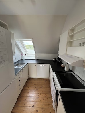A compact kitchen with a skylight, wooden flooring, and white cabinetry. - Det Gamle Rådhus (Grasten)