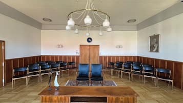 A conference room with a wooden desk, black chairs, a chandelier, and a clock on the wall.