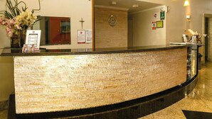 A reception area with a stone-textured counter, a clock, and a cross on the wall. - Hotel Elevado (Porto Alegre)