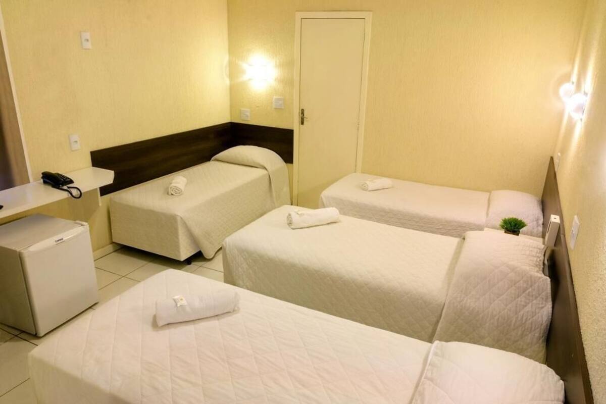 Ein Hotelzimmer mit drei Einzelbetten, einem Schreibtisch mit Telefon und einem kleinen Kühlschrank.