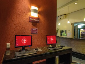 Two computer workstations with monitors displaying the logo of a hotel chain, a sign indicating no smoking, and a sign stating internet access is available for 20 minutes per person. - Hotel Elevado (Porto Alegre)