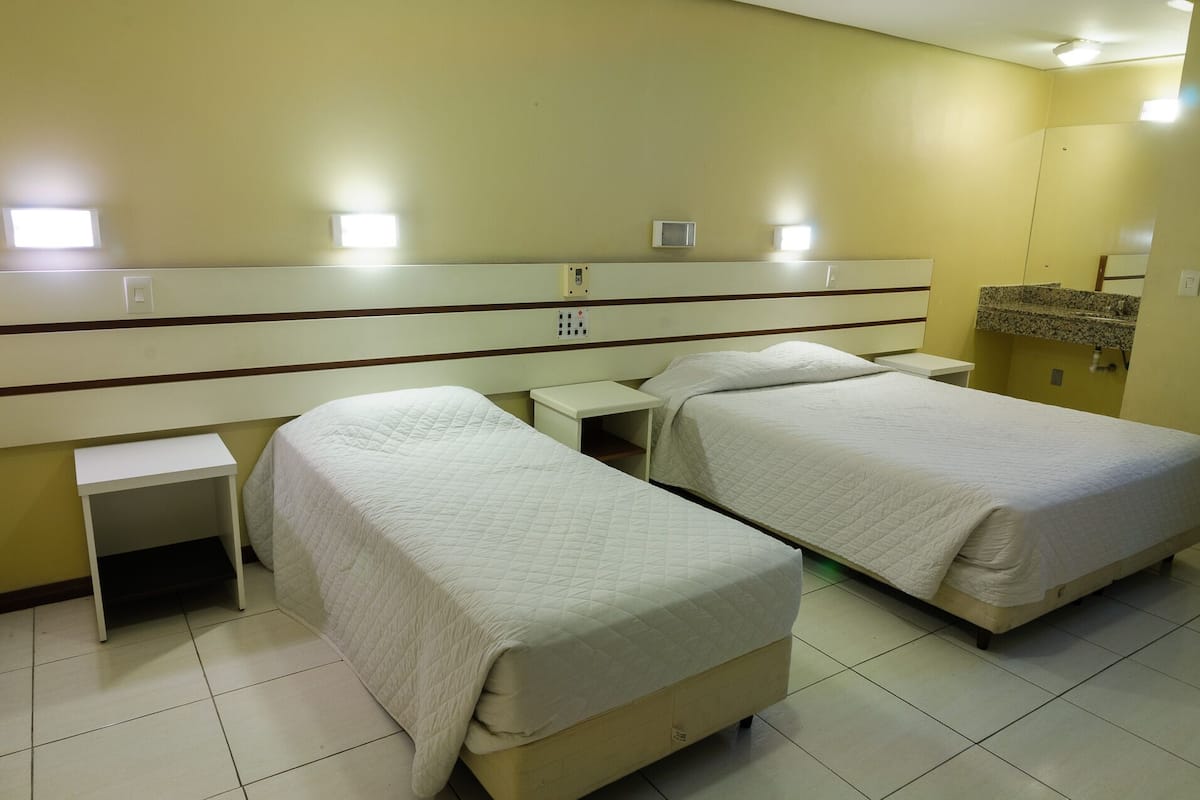 Ein Hotelzimmer mit zwei Betten, einem kleinen Nachttisch, einem Beistelltisch und einer eingebauten Ablage über den Betten.