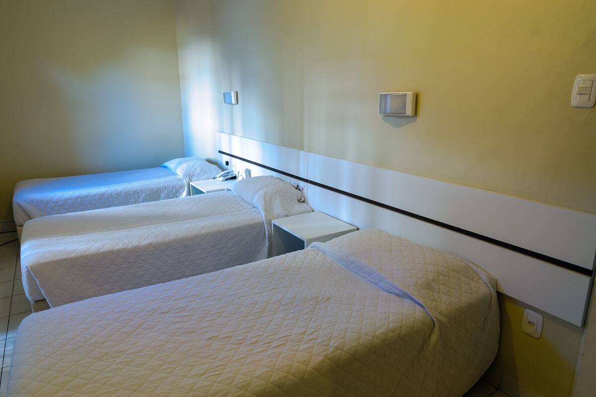 Ein Hotelzimmer mit drei Einzelbetten, einem Nachttisch mit Telefon und einer Wand-Klimaanlage.