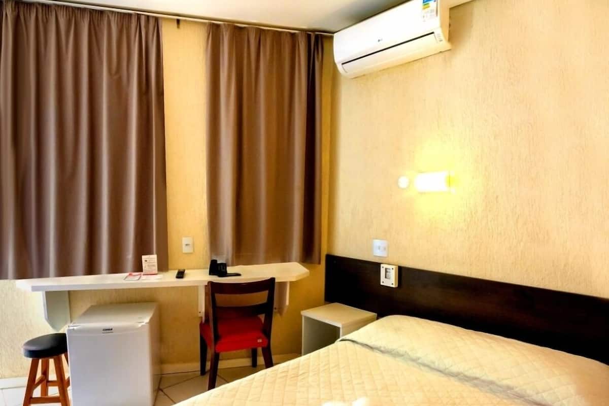 Ein Hotelzimmer mit Bett, Schreibtisch, Stuhl, kleinem Kühlschrank und Klimaanlage.