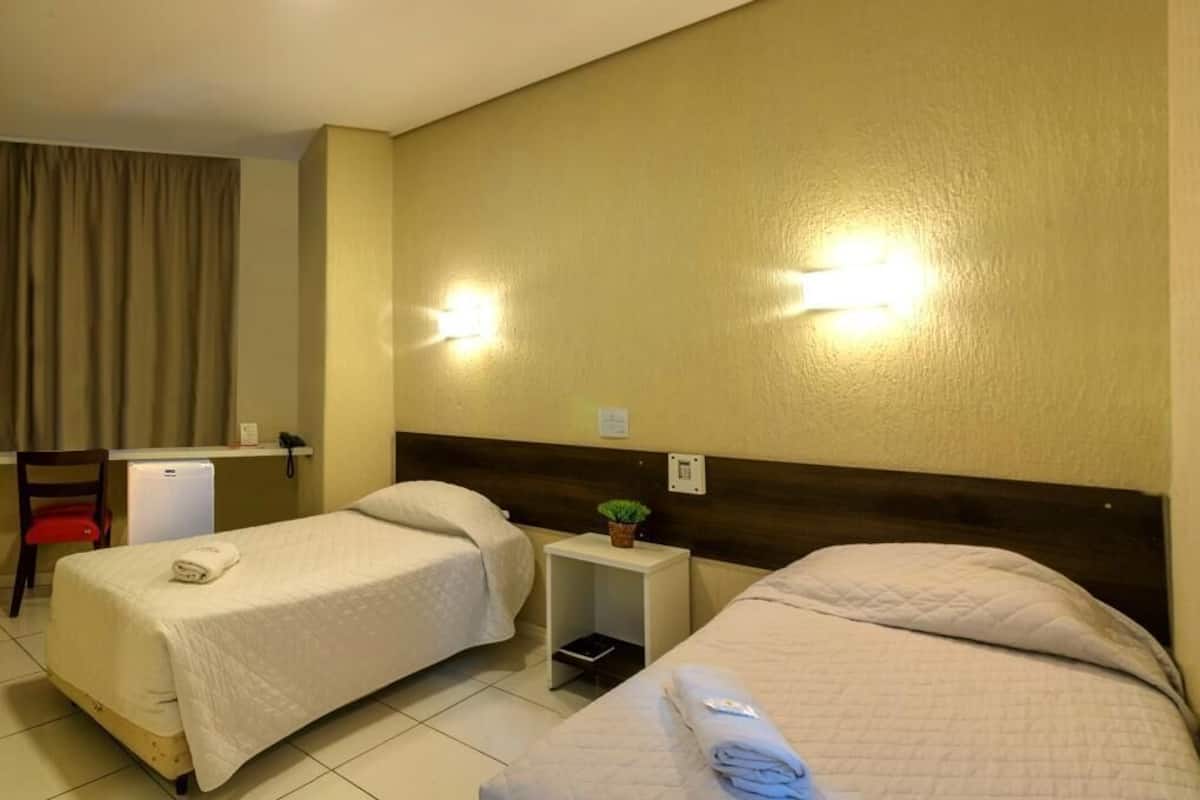 Ein Hotelzimmer mit zwei Betten, einem Schreibtisch, einem Stuhl und einem kleinen Tisch mit einer Pflanze.