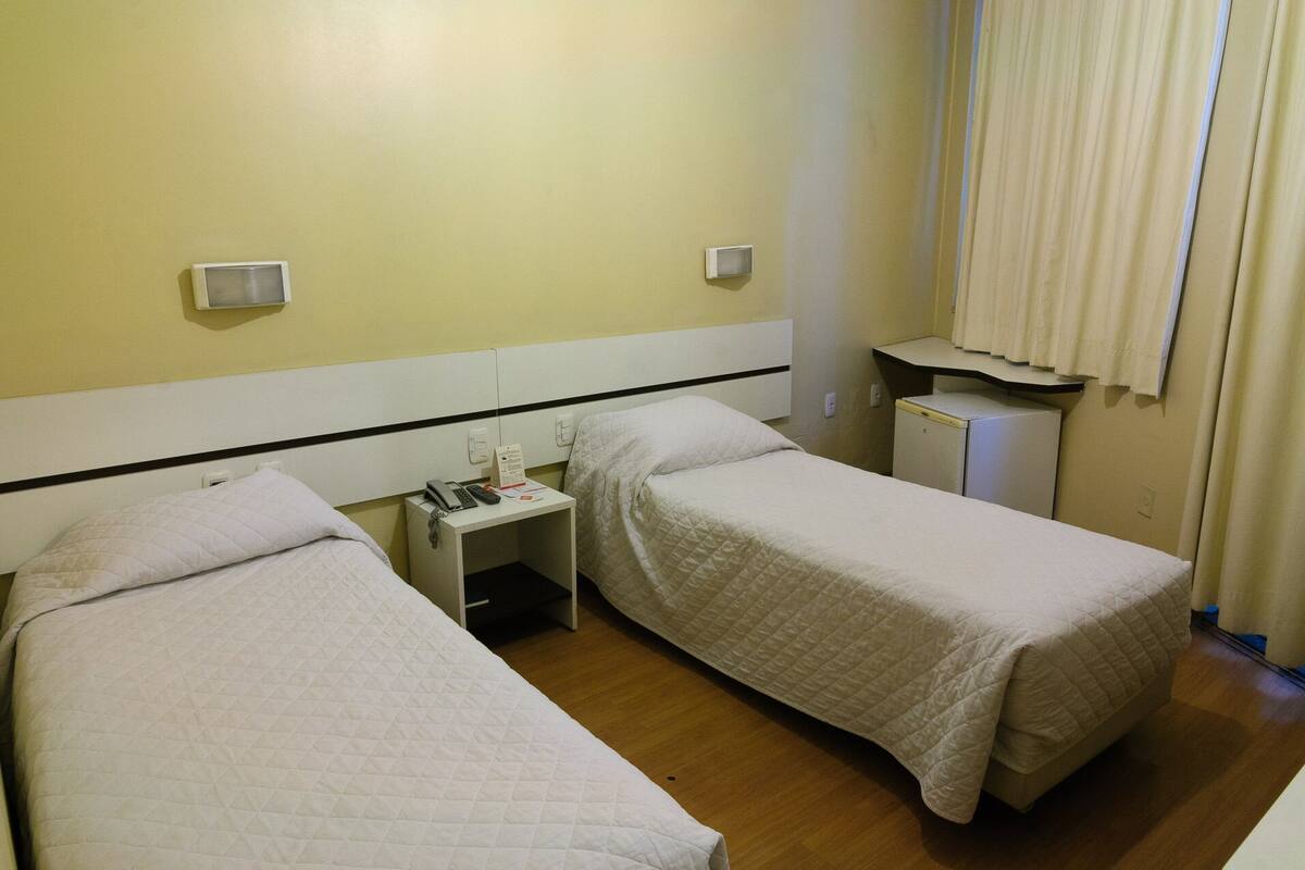 Ein Hotelzimmer mit zwei Betten, einem kleinen Schreibtisch mit Telefon und Papier sowie einem kompakten Kühlschrank.
