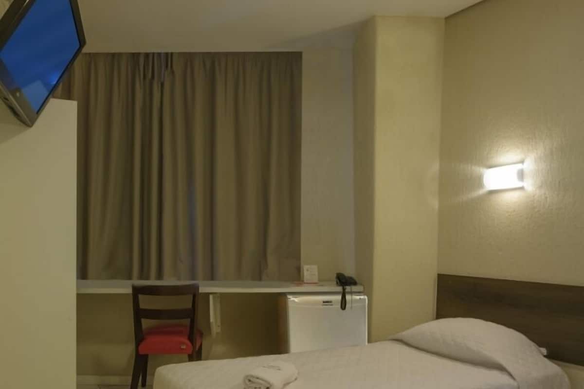 Ein Hotelzimmer mit einem Bett, einem Schreibtisch, einem Stuhl, einem Flachbildfernseher, einem Telefon und einer Wandleuchte.