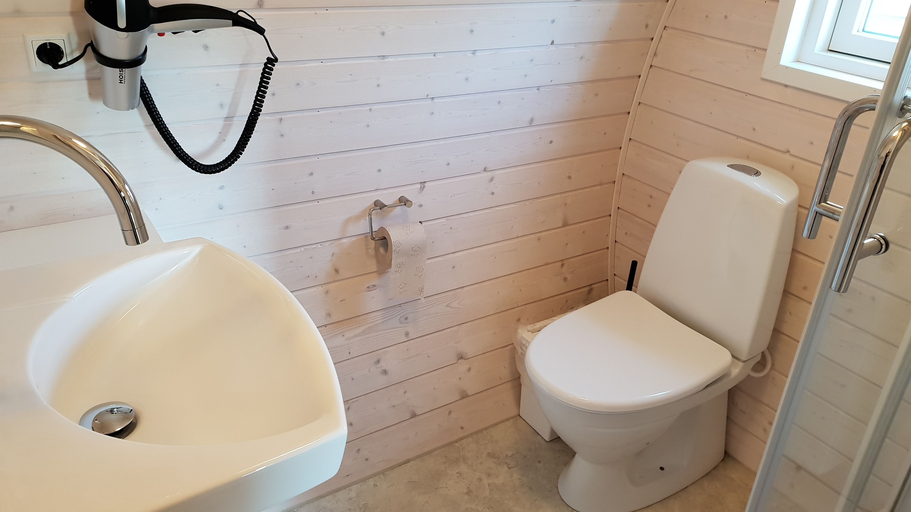Et badeværelse med en hvid vask, toilet og en vægmonteret håndtørrer.