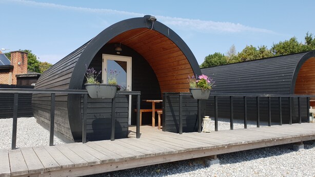 A modern building with a curved wooden roof and black exterior walls. There are two wooden benches and a small table outside. - Hodde Kro (Tistrup)