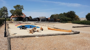 A beach area with a wooden play structure, a rainbow-colored sandbox, and a wooden boat. - Hodde Kro (Tistrup)