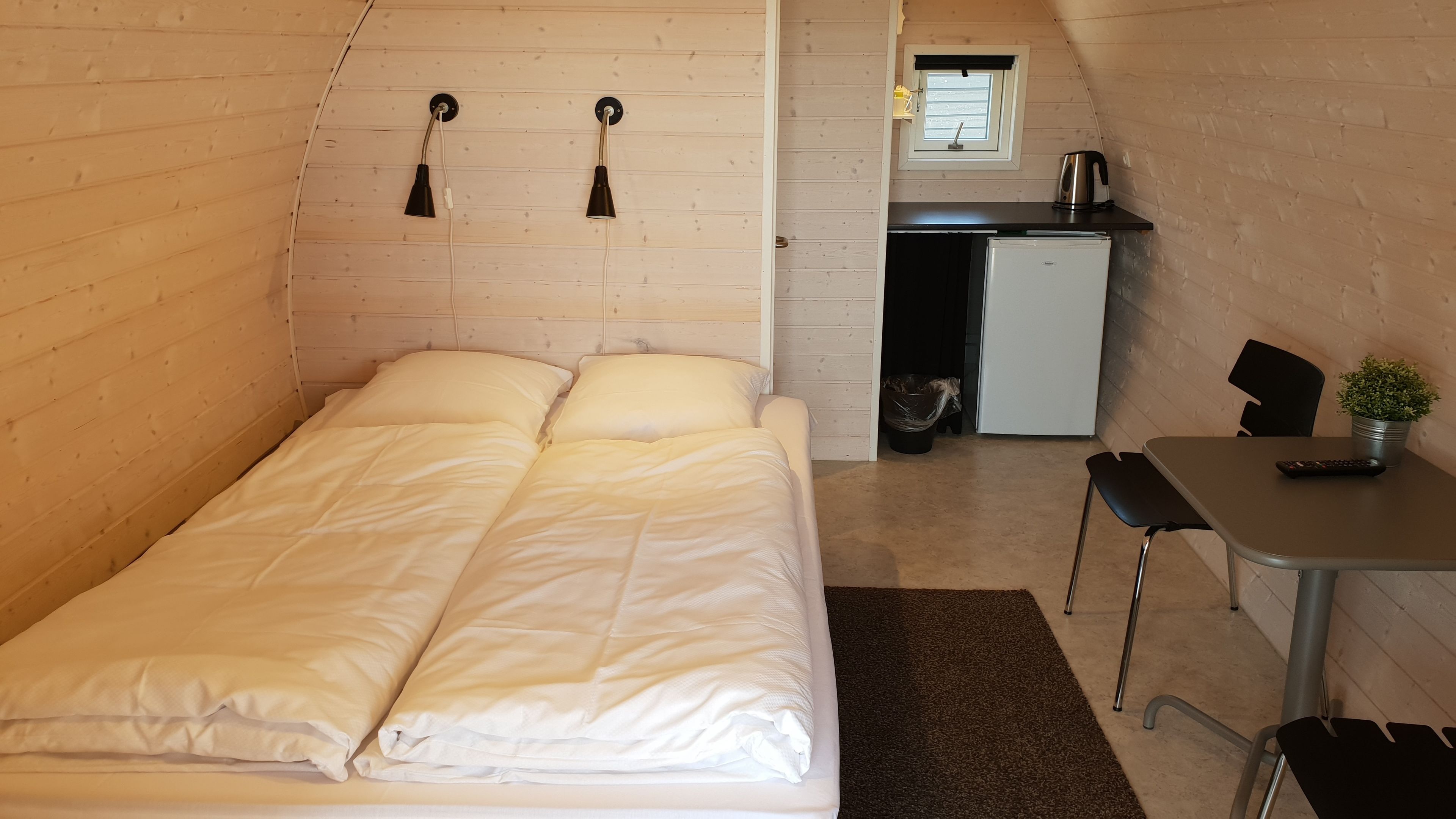 A compact bedroom with a bed, a desk, and a small kitchenette.