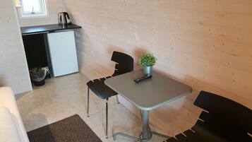 Ett kompakt kök med ett kylskåp, en vattenkokare och ett litet bord med en krukväxt.