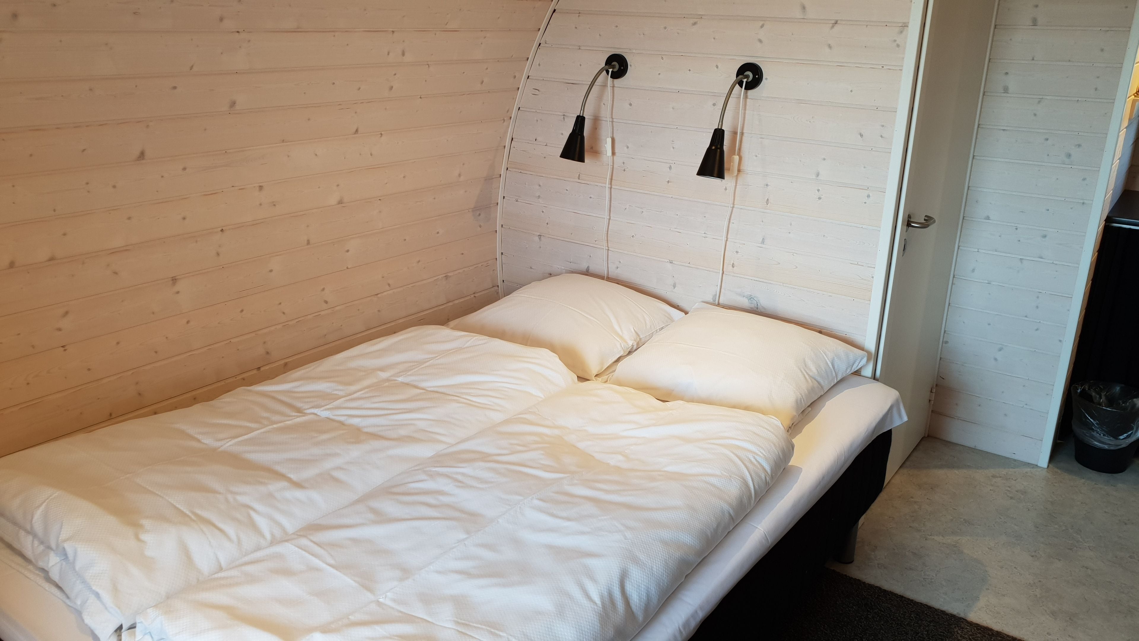Una cama individual con ropa de cama blanca y dos lámparas de pared.