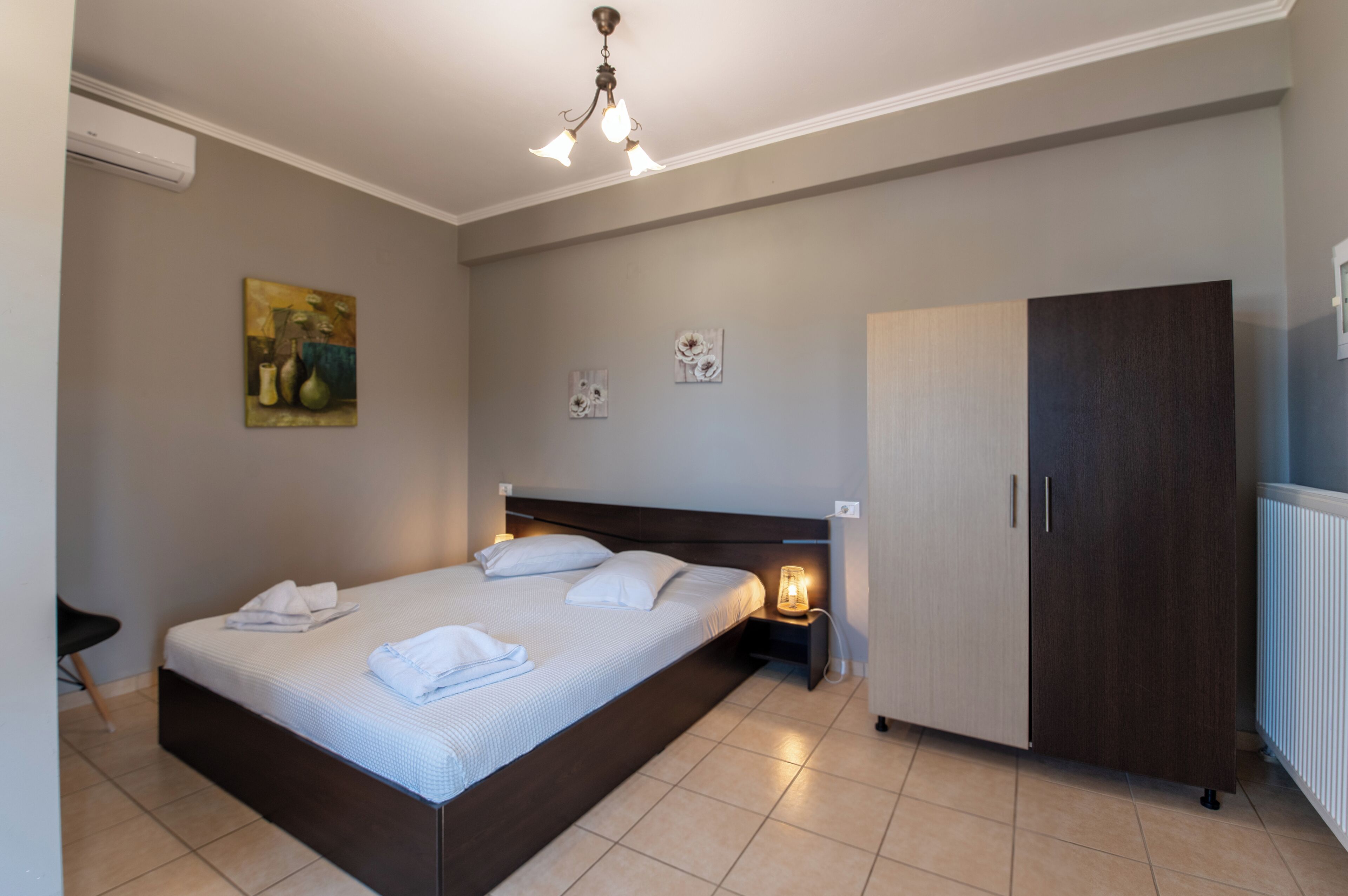 A bedroom with a bed, bedside table, lamp, wardrobe, and artwork on the wall.