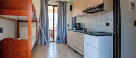 A compact room with a bunk bed, kitchenette, and a sliding door leading to a balcony.