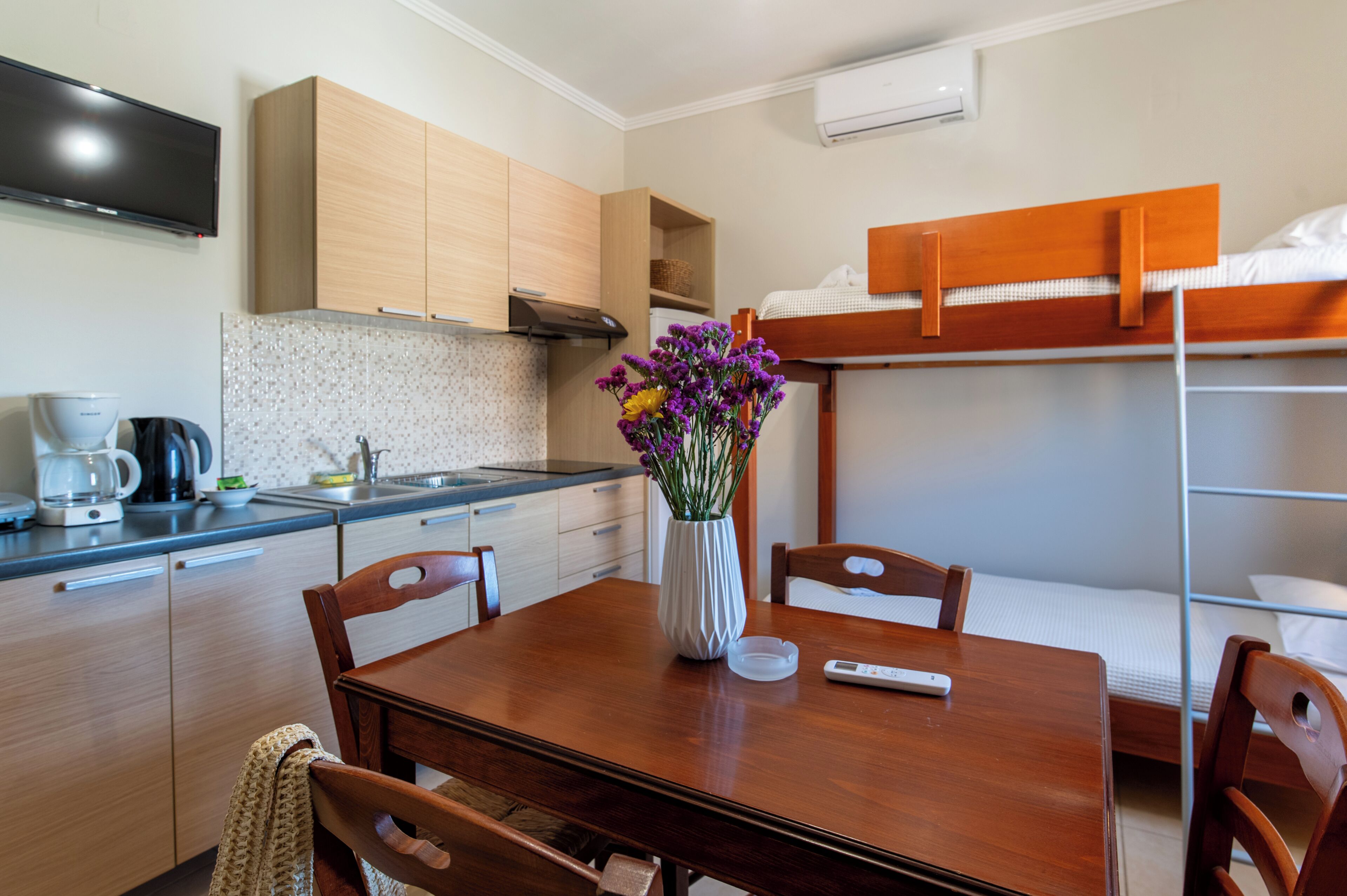 Habitación de hotel pequeña con kitchenette, una mesa de comedor con sillas, una cama individual y un baño compacto.