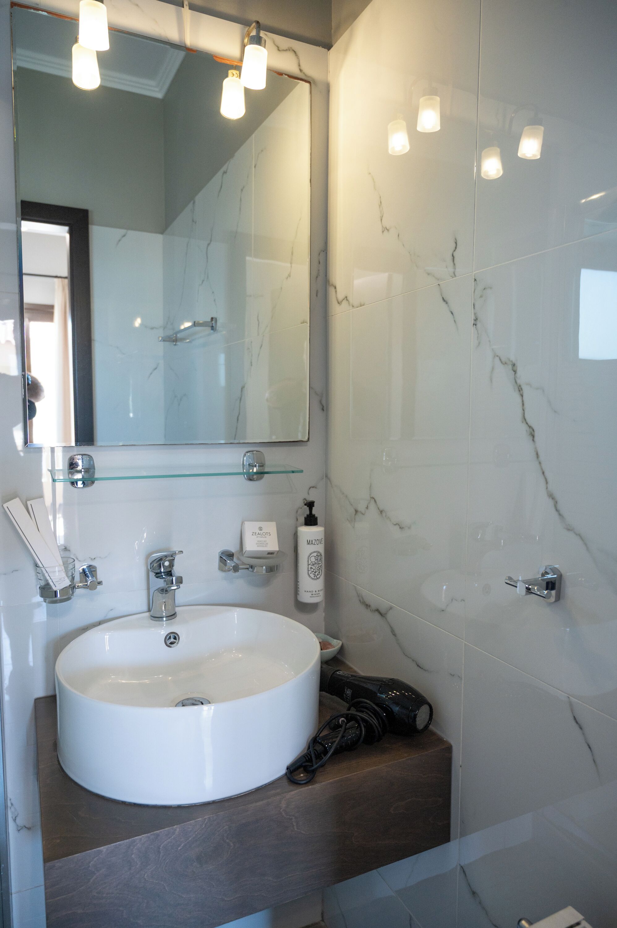 A bathroom with a marble sink, a glass shelf, a mirror, and a handheld hair dryer.