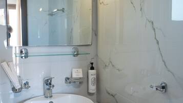 A bathroom with a marble sink, a glass shelf, a mirror, and a handheld hair dryer.