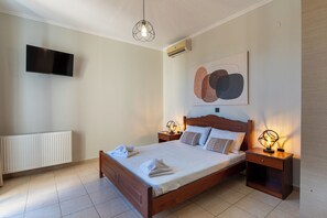 A bedroom with a bed, bedside lamps, a wall-mounted TV, and an air conditioning unit.