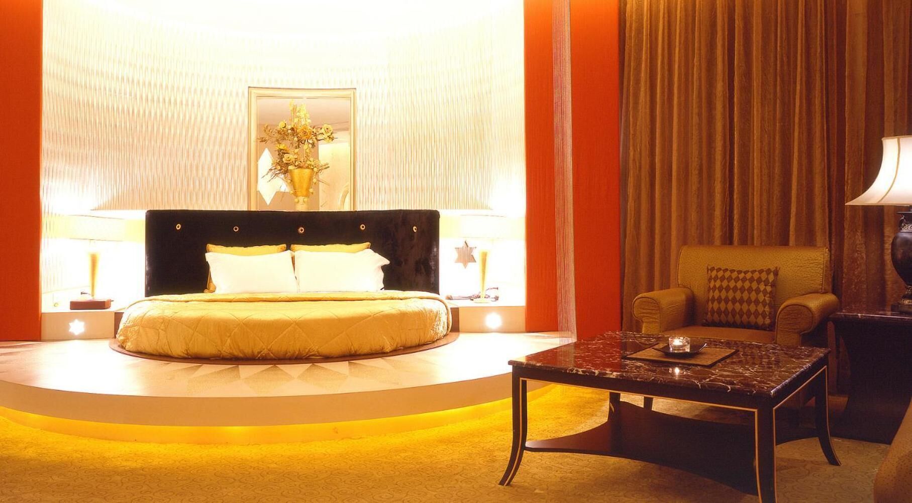 A hotel room with a large bed, a round coffee table, a sofa, and a chandelier.