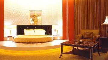 A hotel room with a large bed, a round coffee table, a sofa, and a chandelier.