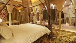 A luxurious bedroom with a canopy bed, ornate decor, and a large mirror.