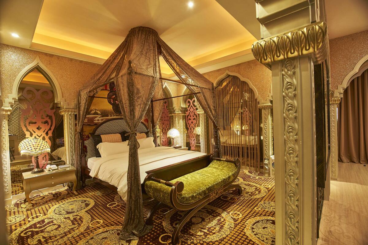Een luxueuze slaapkamer met een hemelbed, decoratieve gordijnen en een kamerbreed tapijt met patroon.
