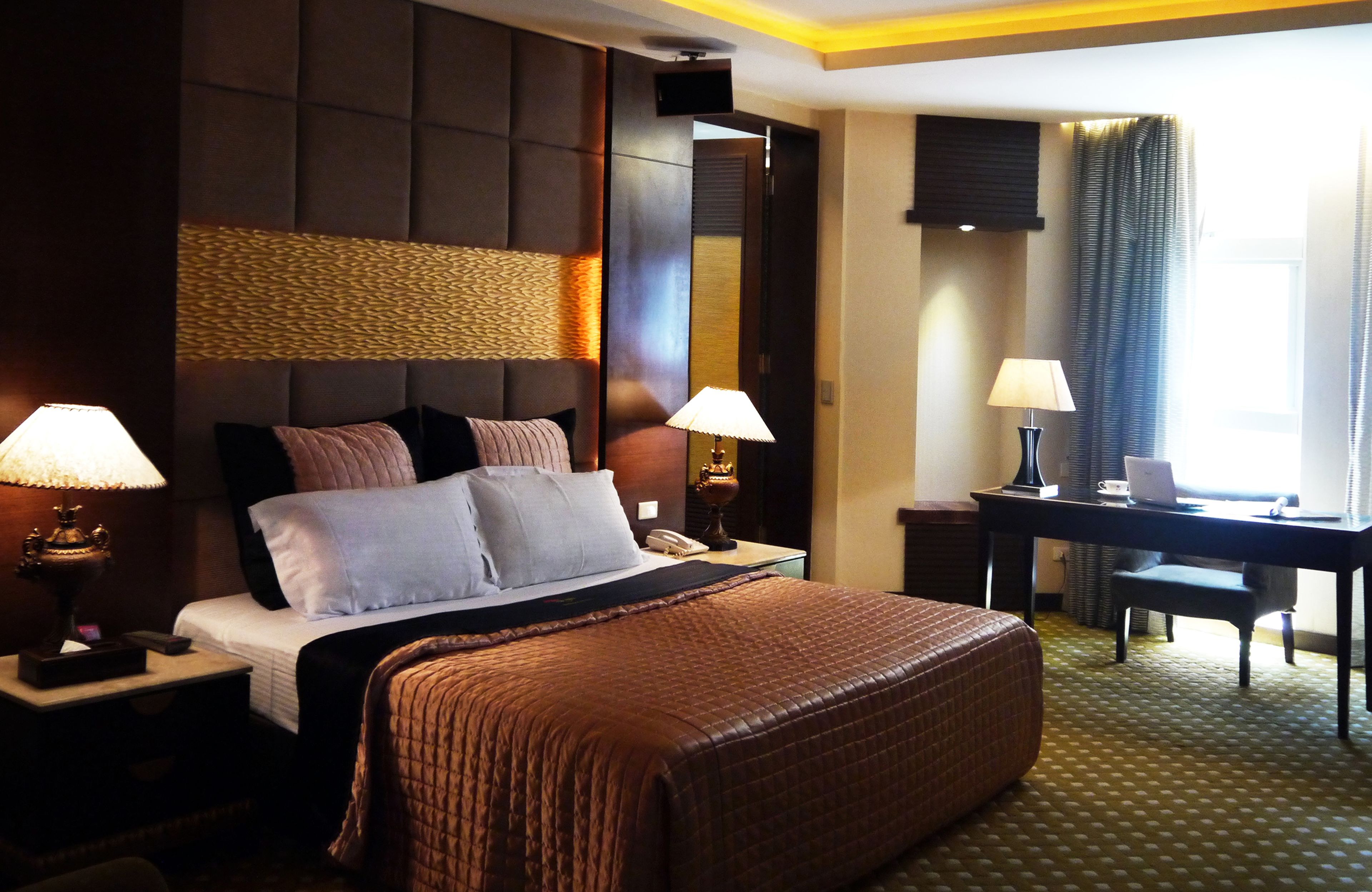 A hotel room with a large bed, two bedside tables with lamps, a desk, and a chair.